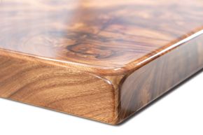 Close-up of a glossy wood tabletop corner with rounded edge and swirling grain pattern