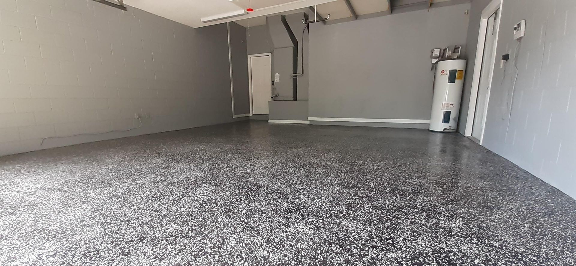 A garage with a gray floor and a water heater.