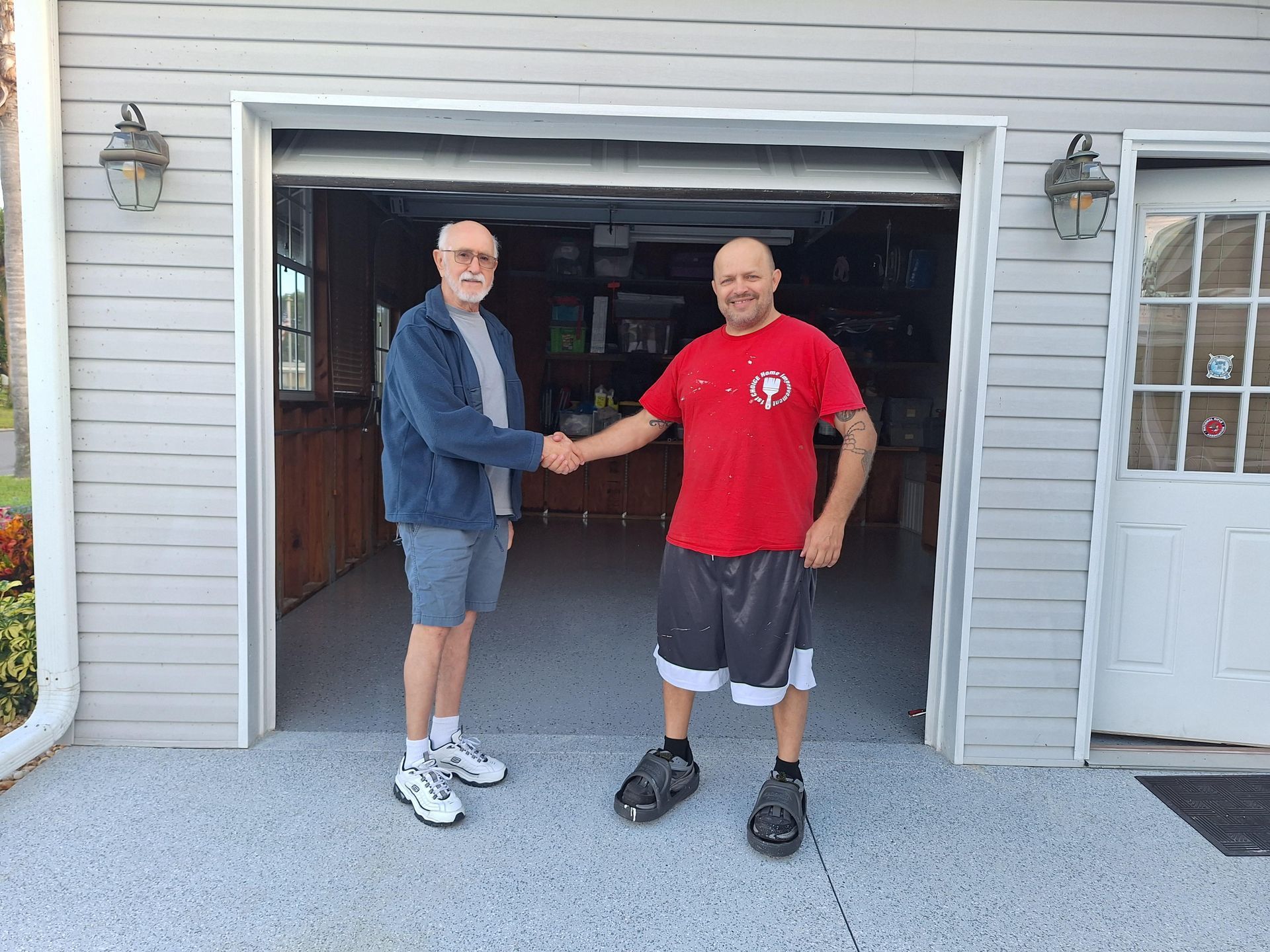 Two men are shaking hands in front of a garage door.