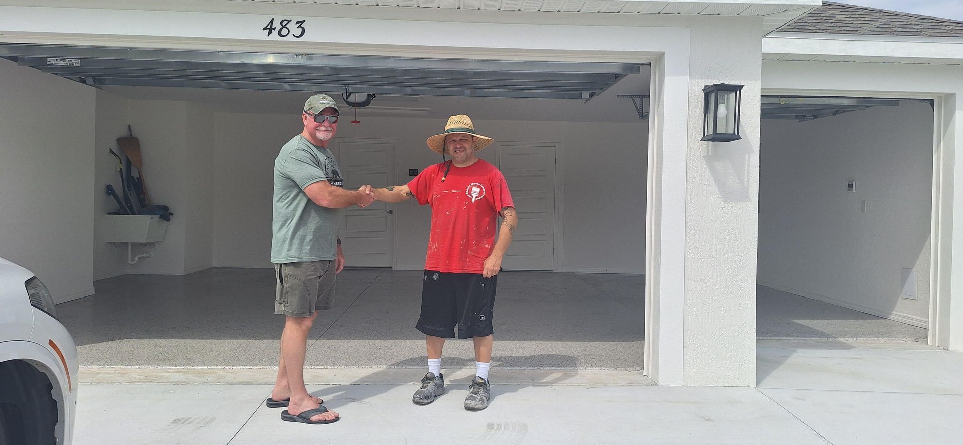 Two men are shaking hands in front of a garage.