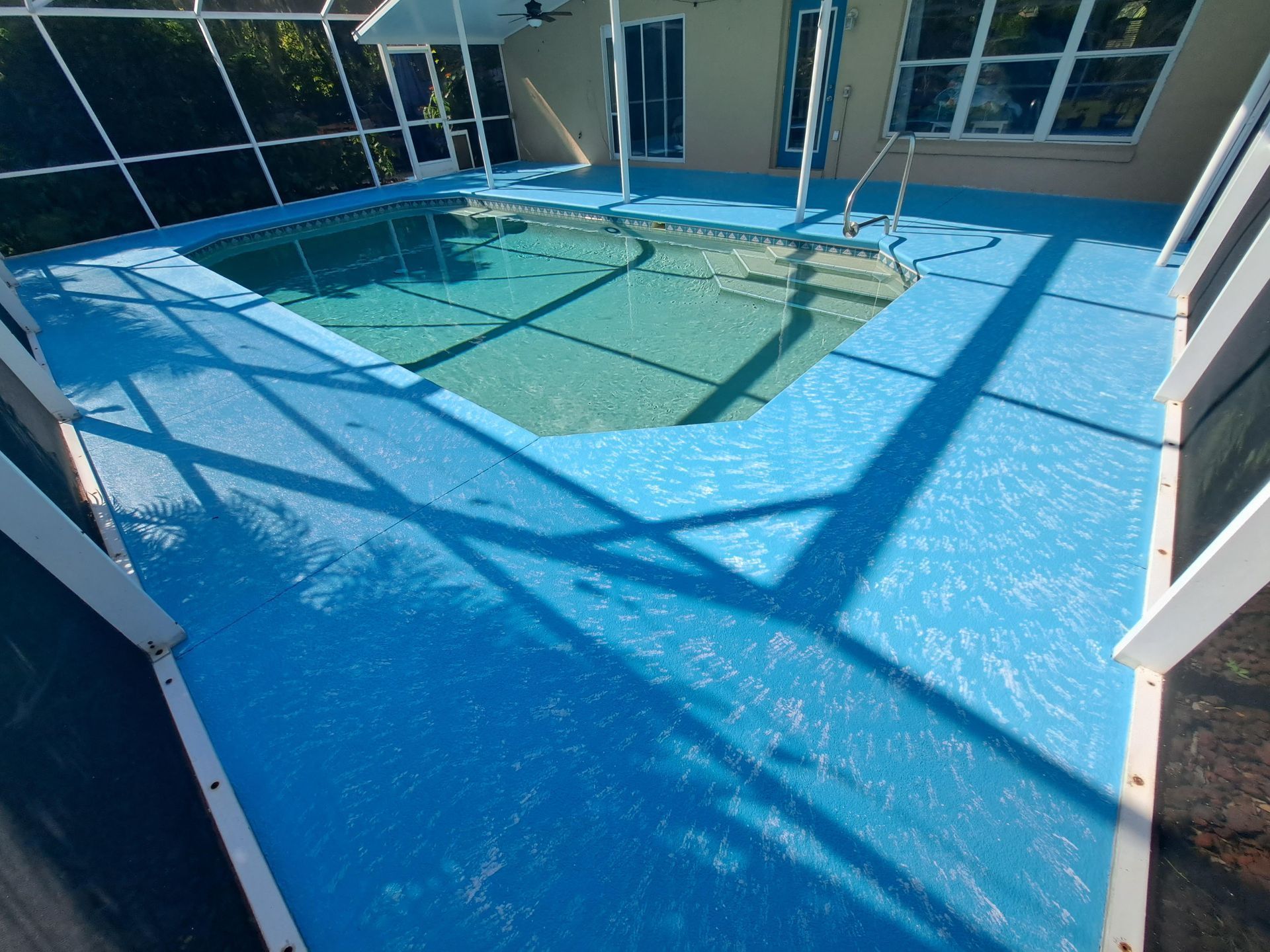 A swimming pool with a blue floor and a screened in area.