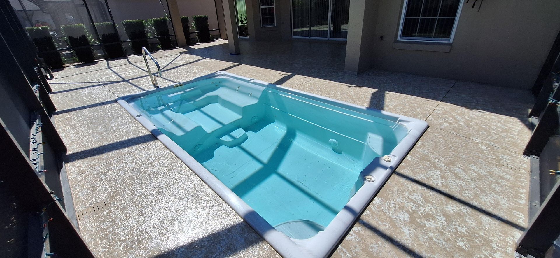 A small swimming pool is sitting on a patio next to a house.