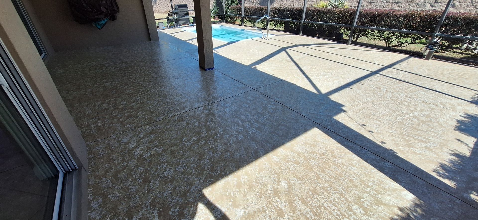 A patio with a sliding glass door and a pool in the background.