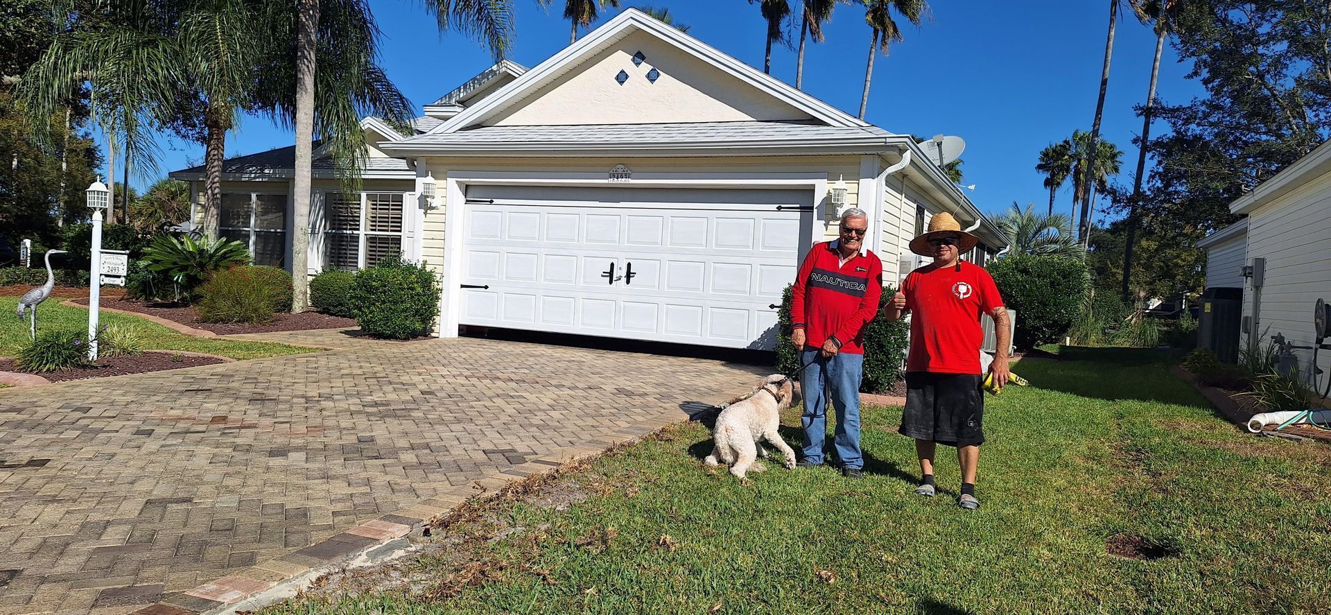 Two men and a dog are standing in front of a house.