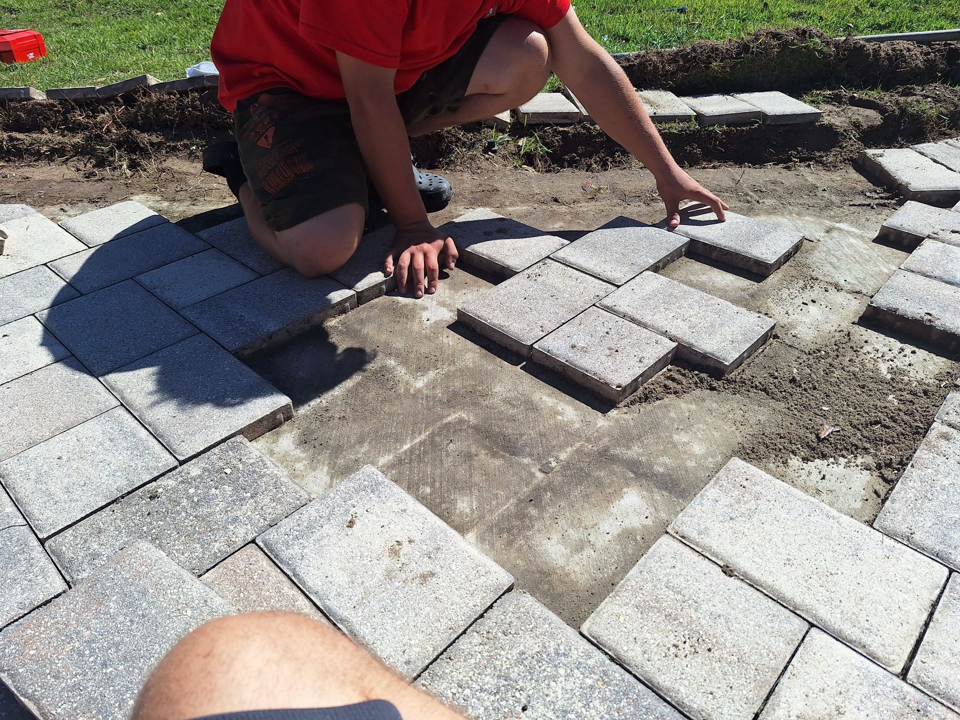 A man in a red shirt is laying bricks on the ground