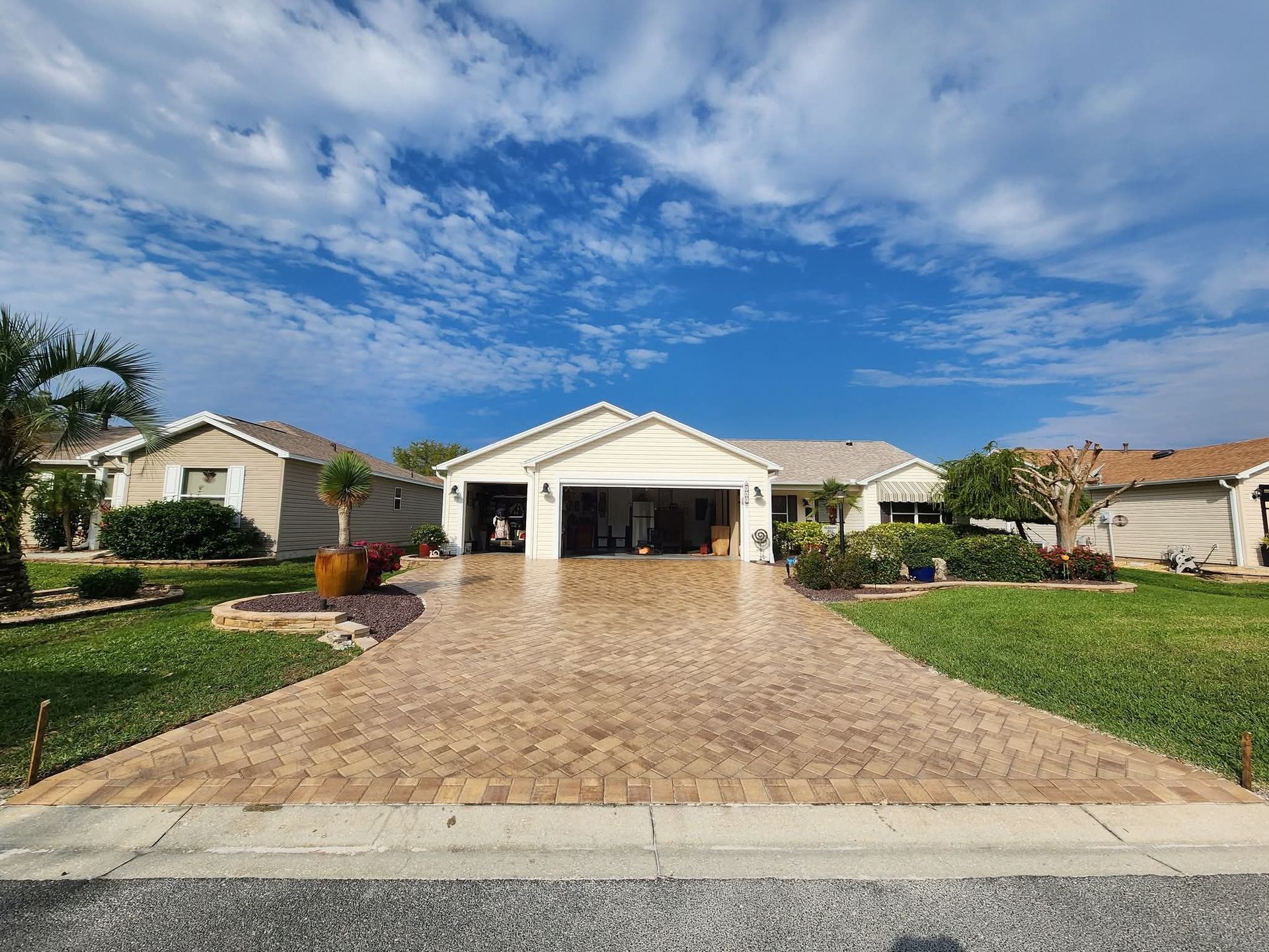 A man is working on a brick driveway in front of a house.