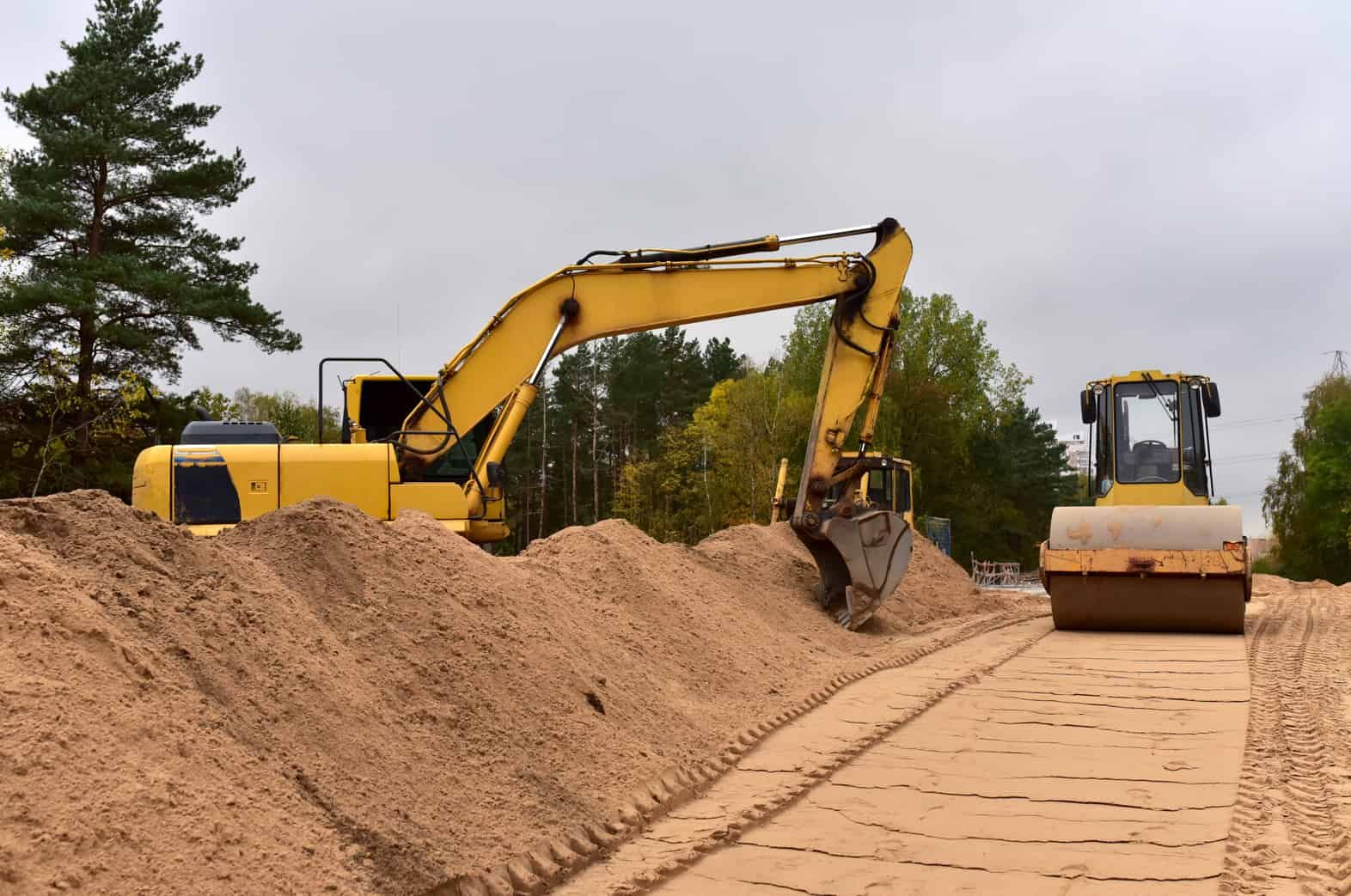 A Yellow Excavator and a Roller Are Working on a Dirt Road — Ensbey Earthmoving in Glenview, QLD