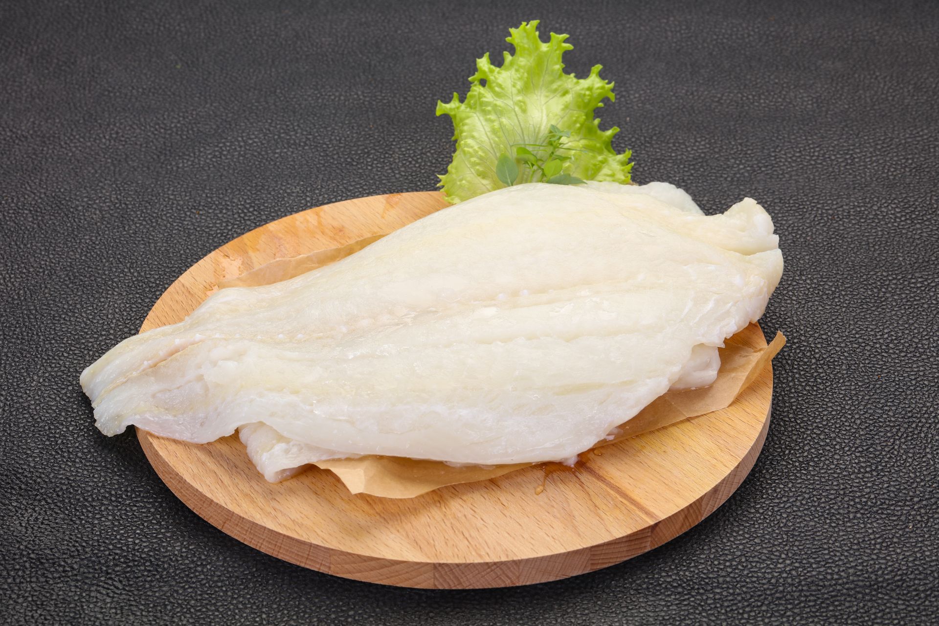 Raw white fish fillet on a wooden plate with lettuce garnish