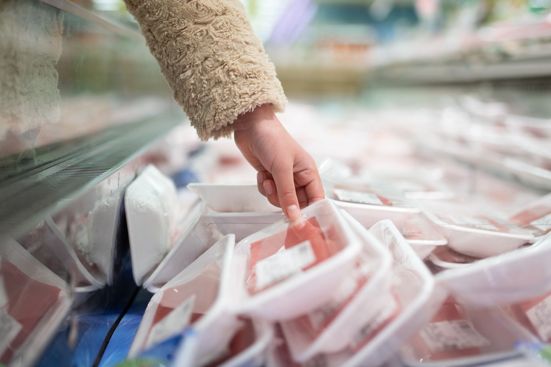 Hand reaching into a market bin of packaged frozen food boxes