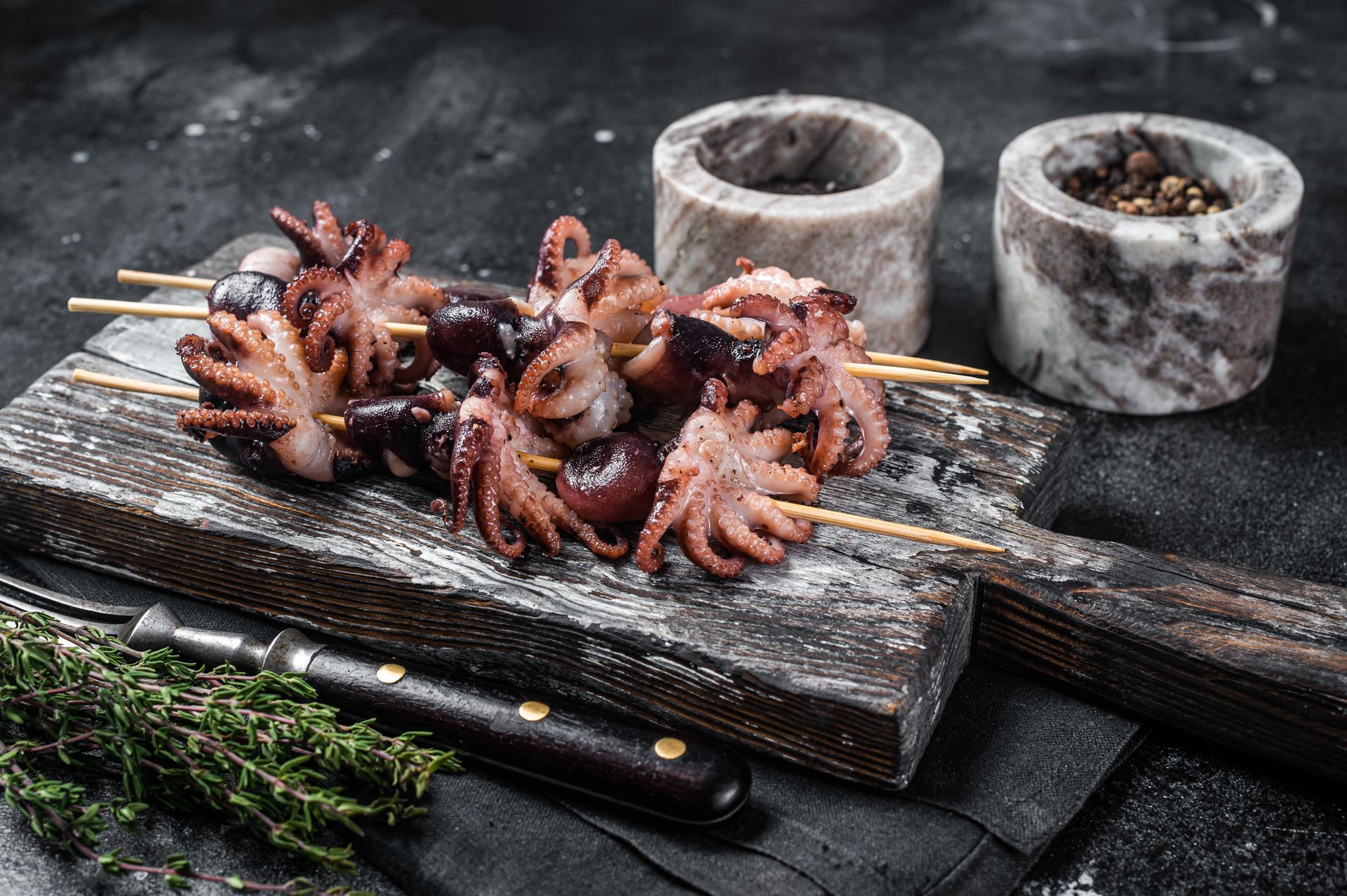 Cooked octopus on skewers, served on a wooden chopping board, next to a knife and rosemary