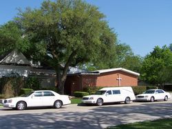 Church with three parked cars along the street under a large tree