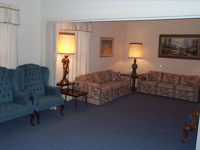 Living room with blue sofa, patterned daybeds, and two lit lamps on a blue carpet