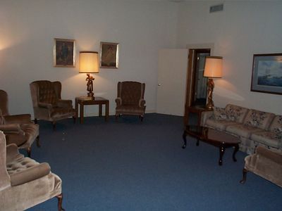 Empty hotel lobby with beige armchairs, floral sofa, lamps, and blue carpet