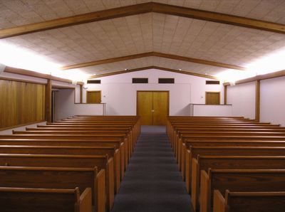 Empty church sanctuary with wooden pews, central aisle, and double doors at the front