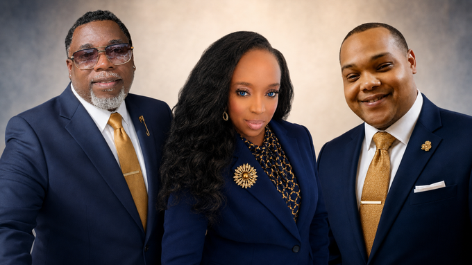Three professionals in navy suits pose against a blue studio backdrop