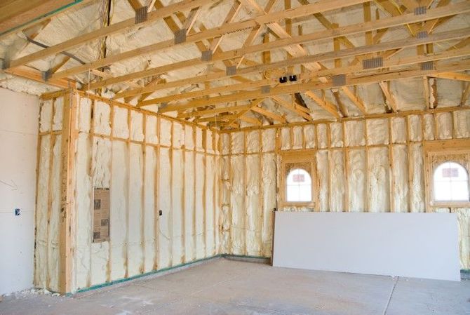 Unfinished interior of a house with exposed wooden framing, white insulated walls, and bare concrete floor.