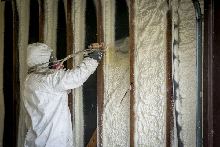 Worker spraying foam insulation inside wall framing