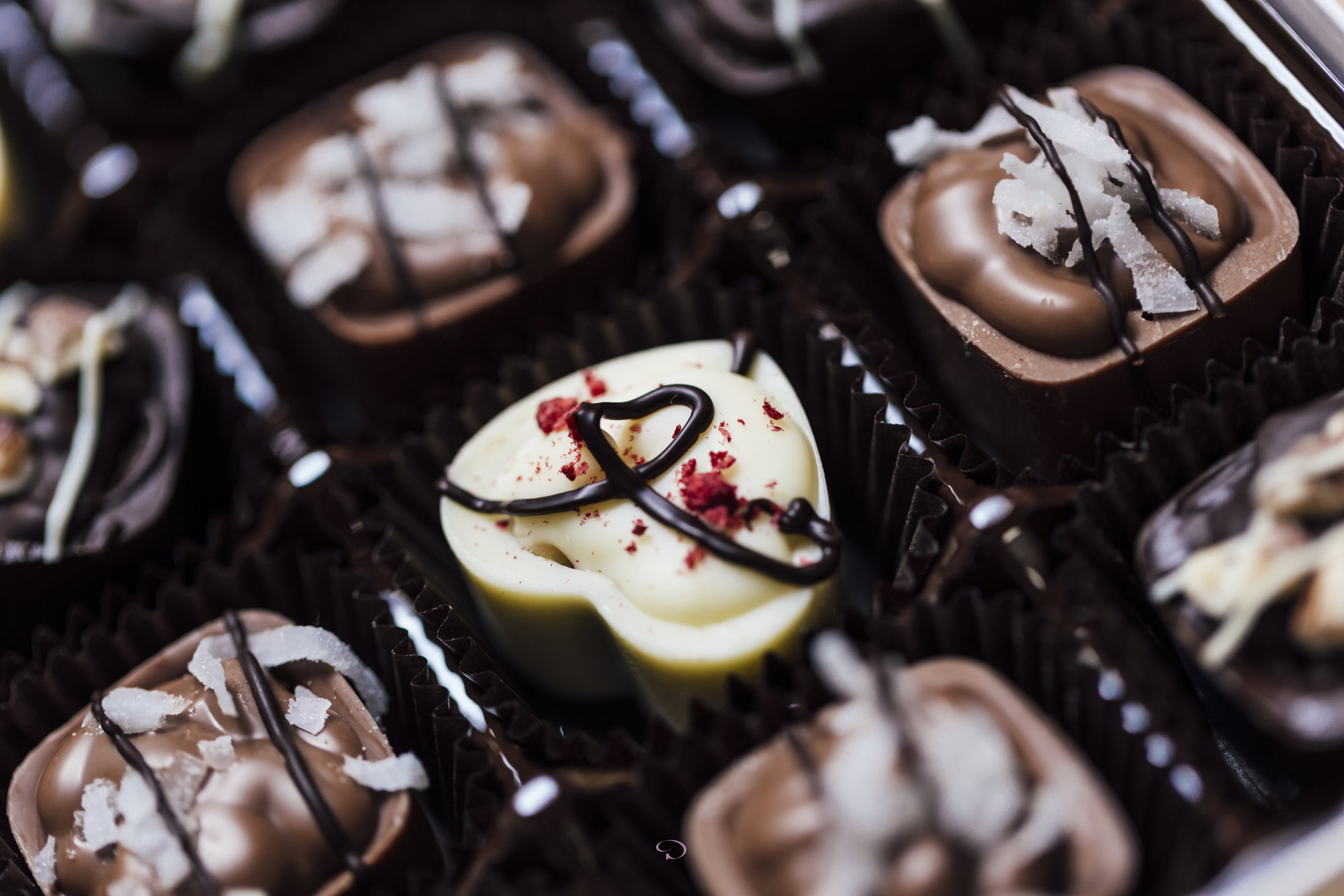 Assorted chocolate truffles in dark paper cups, topped with white and dark drizzle and crushed nuts