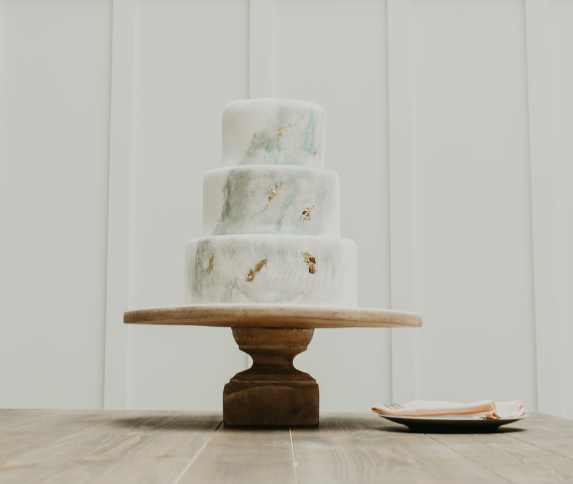 Three-tier white frosted cake on a wooden stand with a small plate beside it