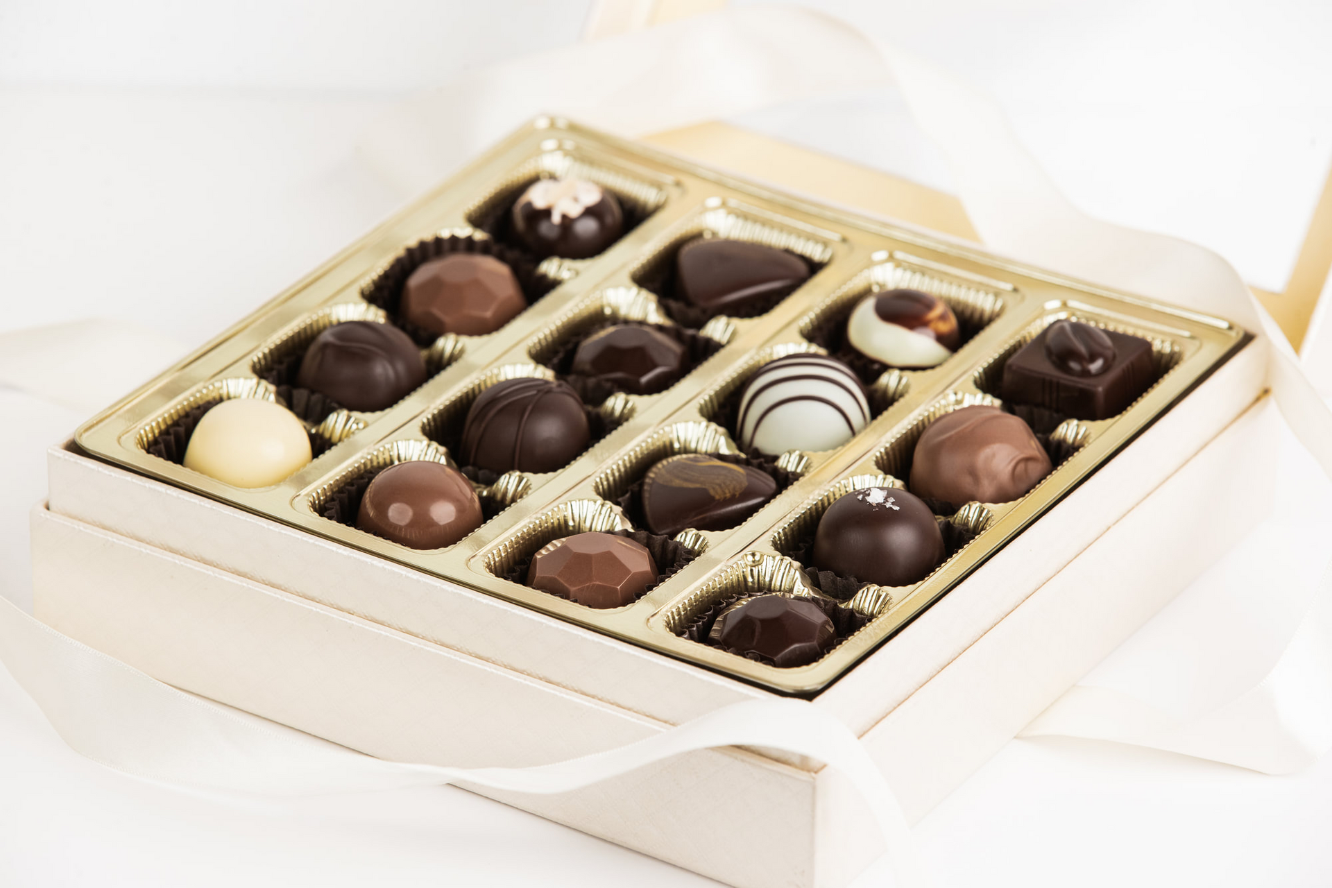 Open box of assorted chocolates in gold packaging on a white background