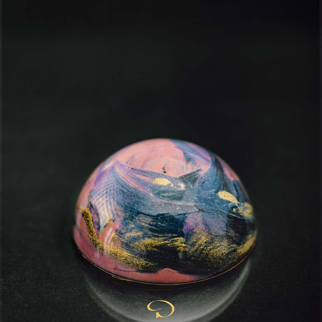 Small iridescent glass dome with pink, blue, and gold swirls on a dark background