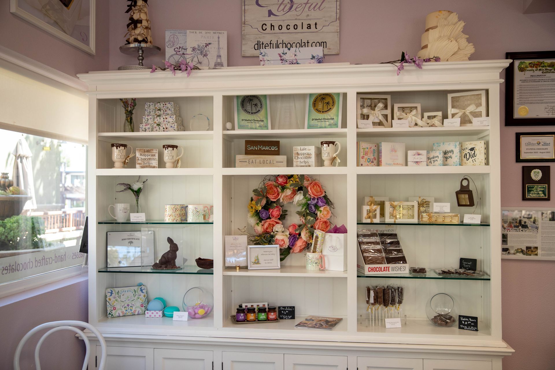White shelves filled with colorful decor, cards, and trinkets in a pastel shop display