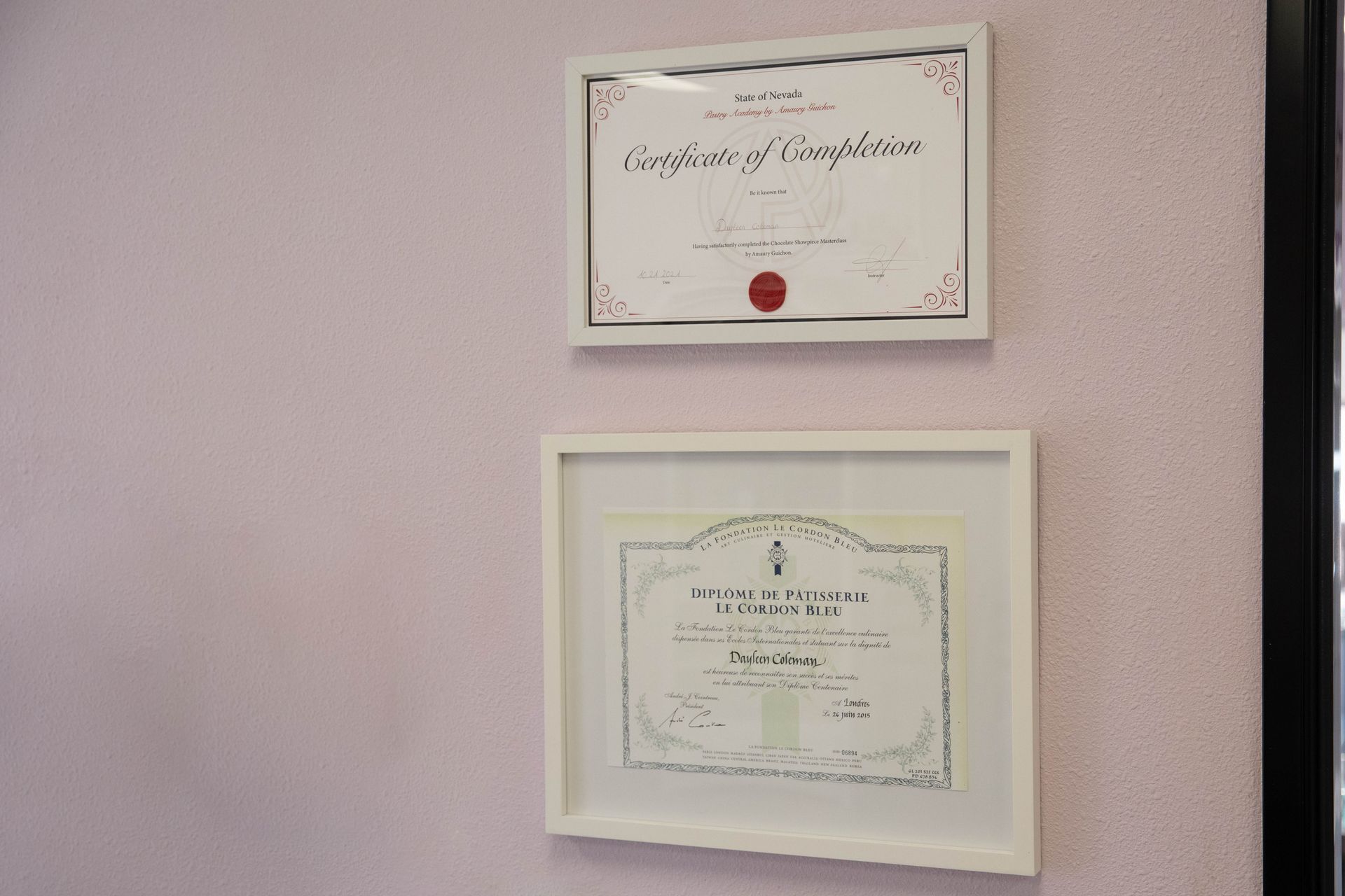 Two framed certificates hanging on a pale pink wall