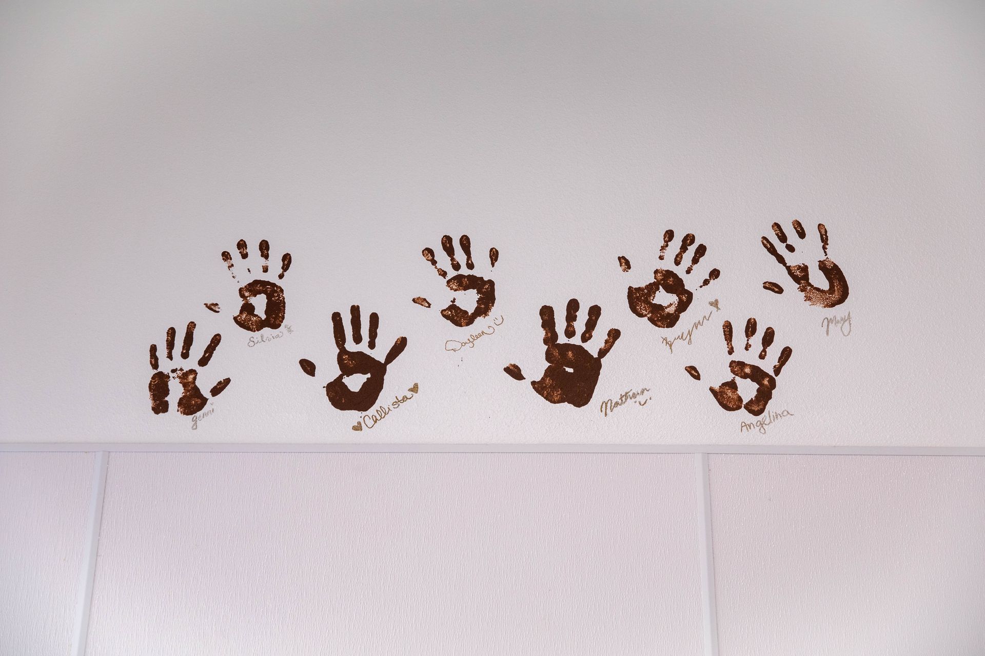 Brown handprints and paw-like prints arranged in a row on a white wall above tiled flooring
