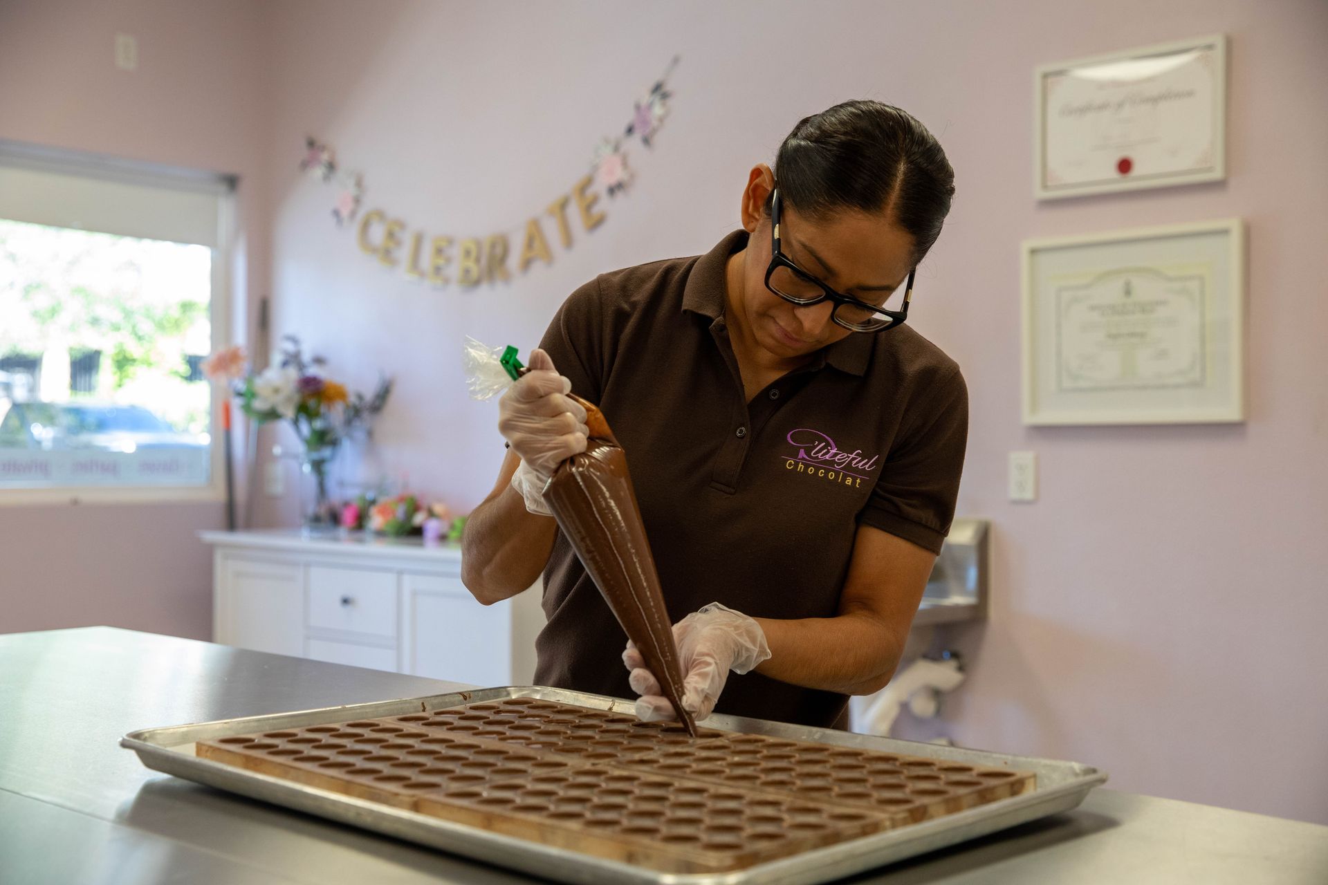 Person decorating a tray of chocolate squares with a piping bag in a bright kitchen.