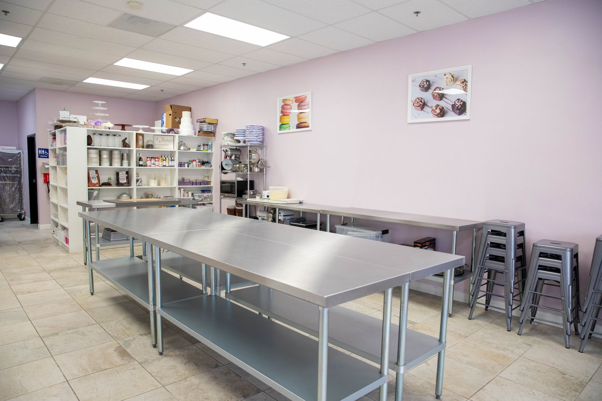 Empty cafeteria with metal tables, stacked chairs, and pale purple walls under bright fluorescent lights
