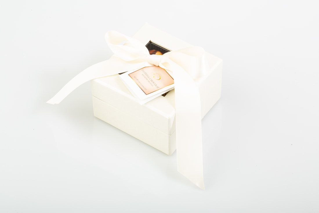 Open white chocolate gift box with four assorted chocolates on a white surface