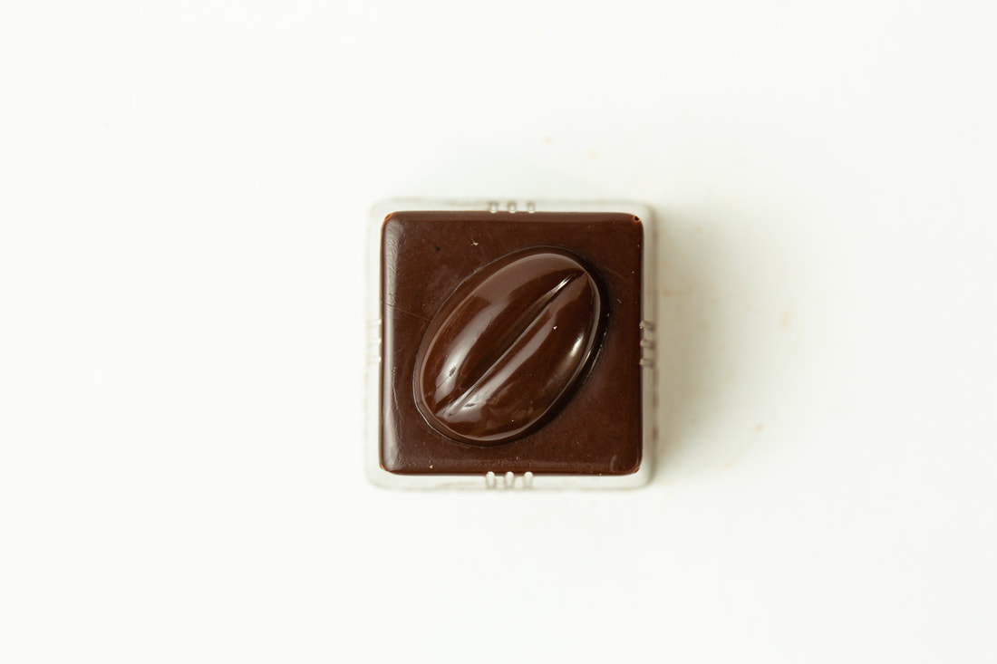 Close-up of a square chocolate candy with a coffee bean design on a white background