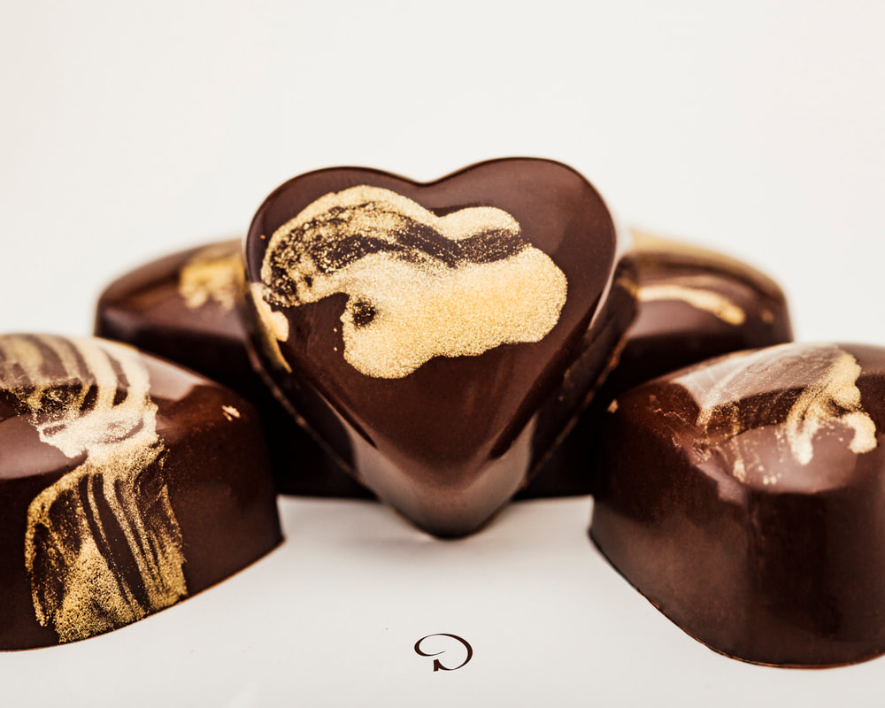Heart-shaped chocolate candies with gold swirls on a white background