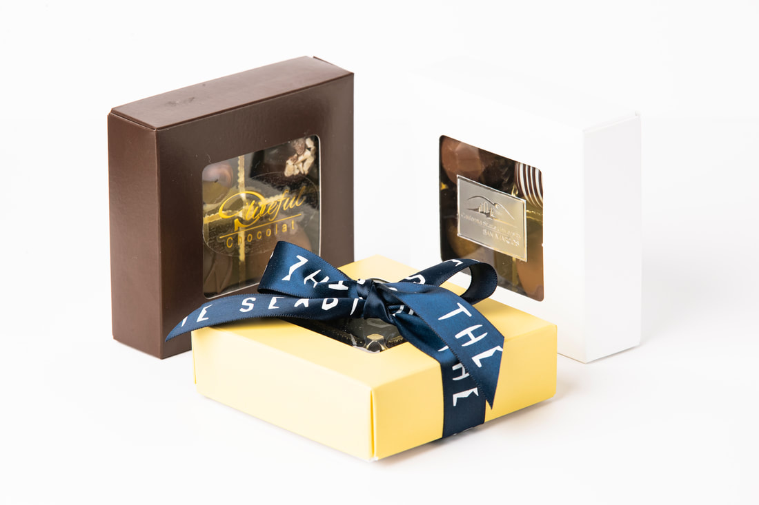 Three wrapped gift boxes with blue ribbon, including brown, gold, and white packaging