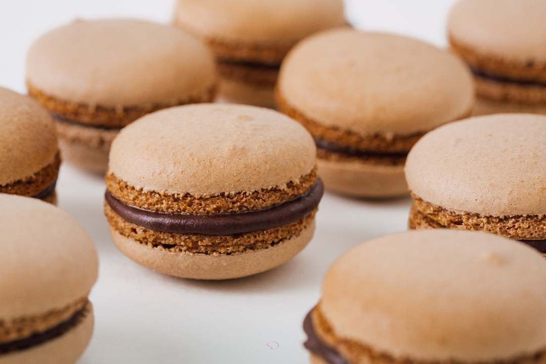 Beige macarons with chocolate filling arranged on a white surface
