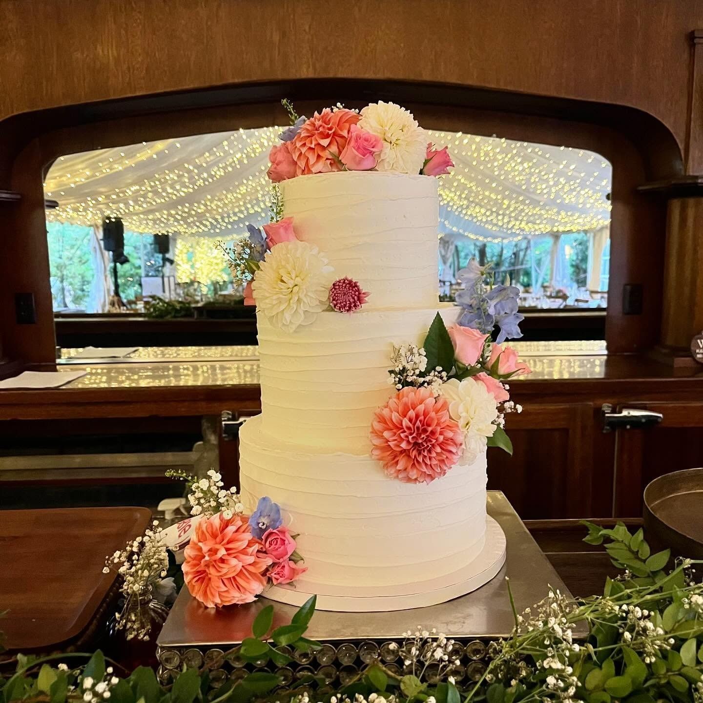 Tall white wedding cake with pink flowers on a table in a wood-paneled venue
