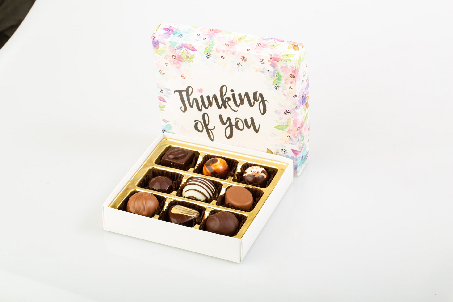 Open gift box of assorted chocolates with “Thinking of you” card in pastel floral packaging