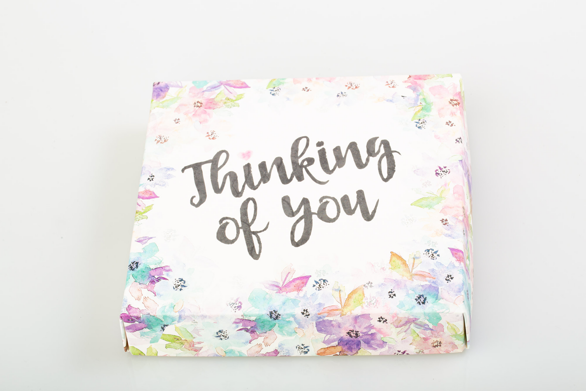 Open gift box of assorted chocolates with “Thinking of you” card in pastel floral packaging