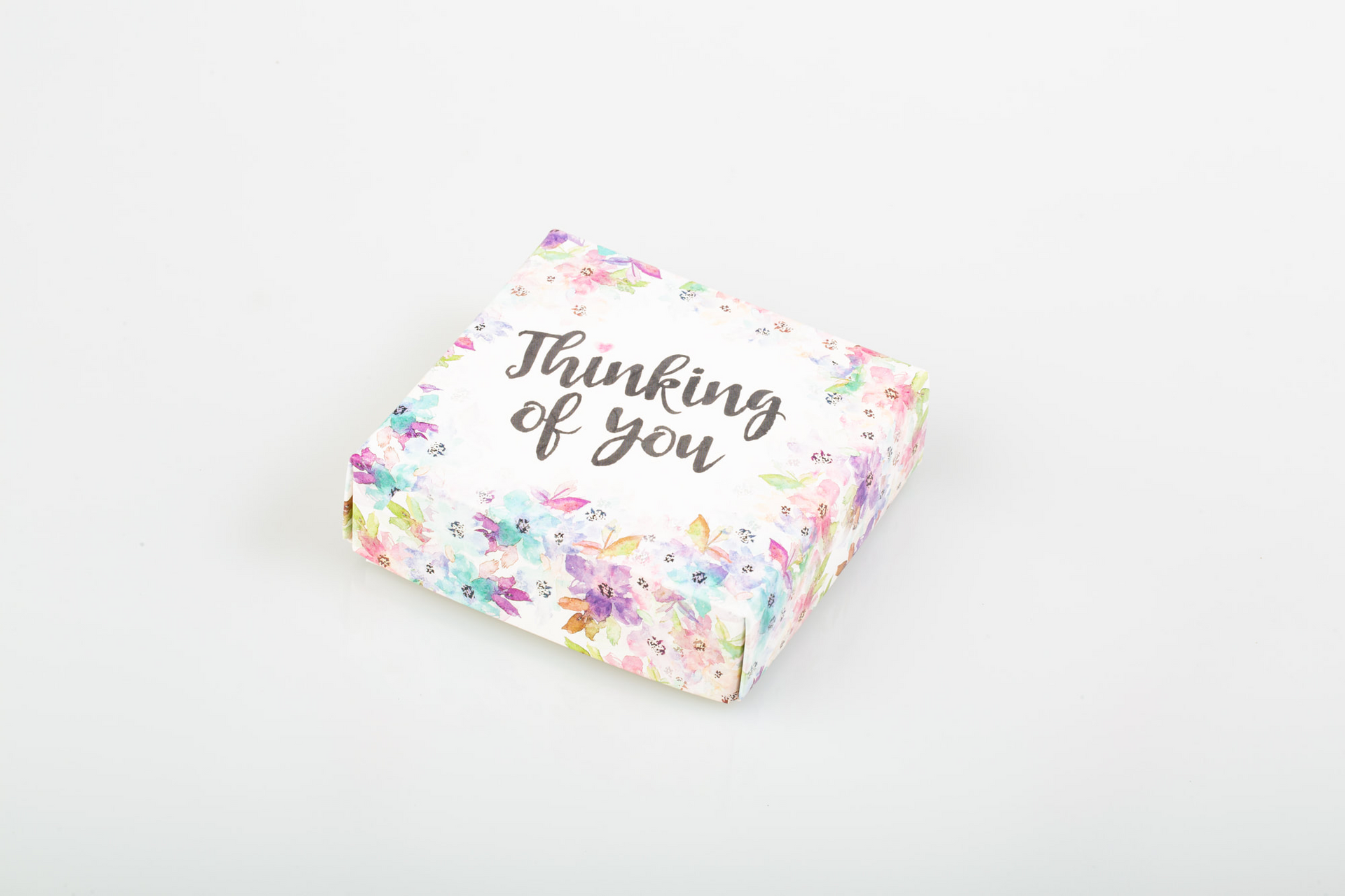 Chocolate gift box with a floral “Thinking of you” card on a white background