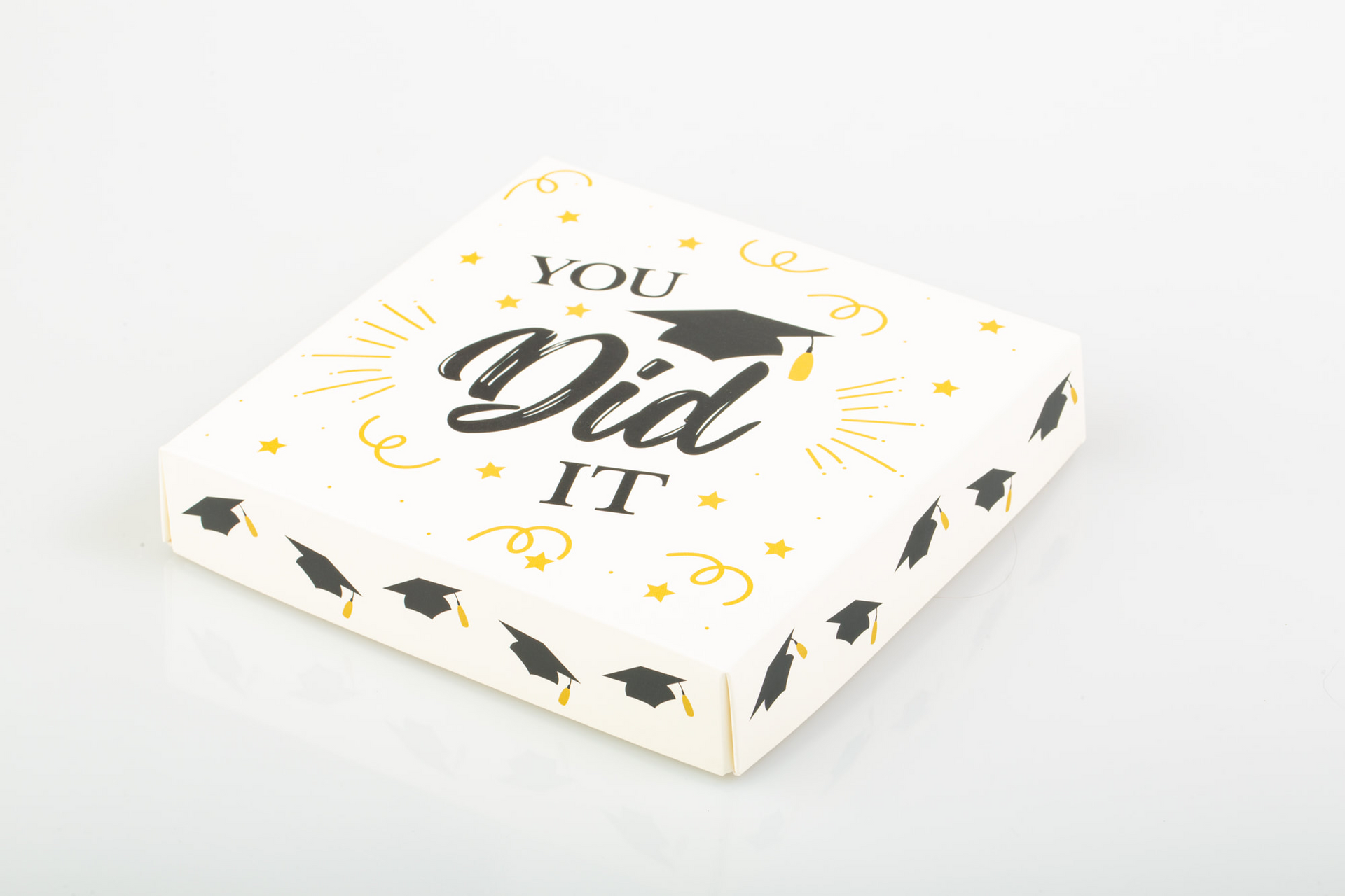 Open box of assorted chocolates with a “You Did It” lid on a white background