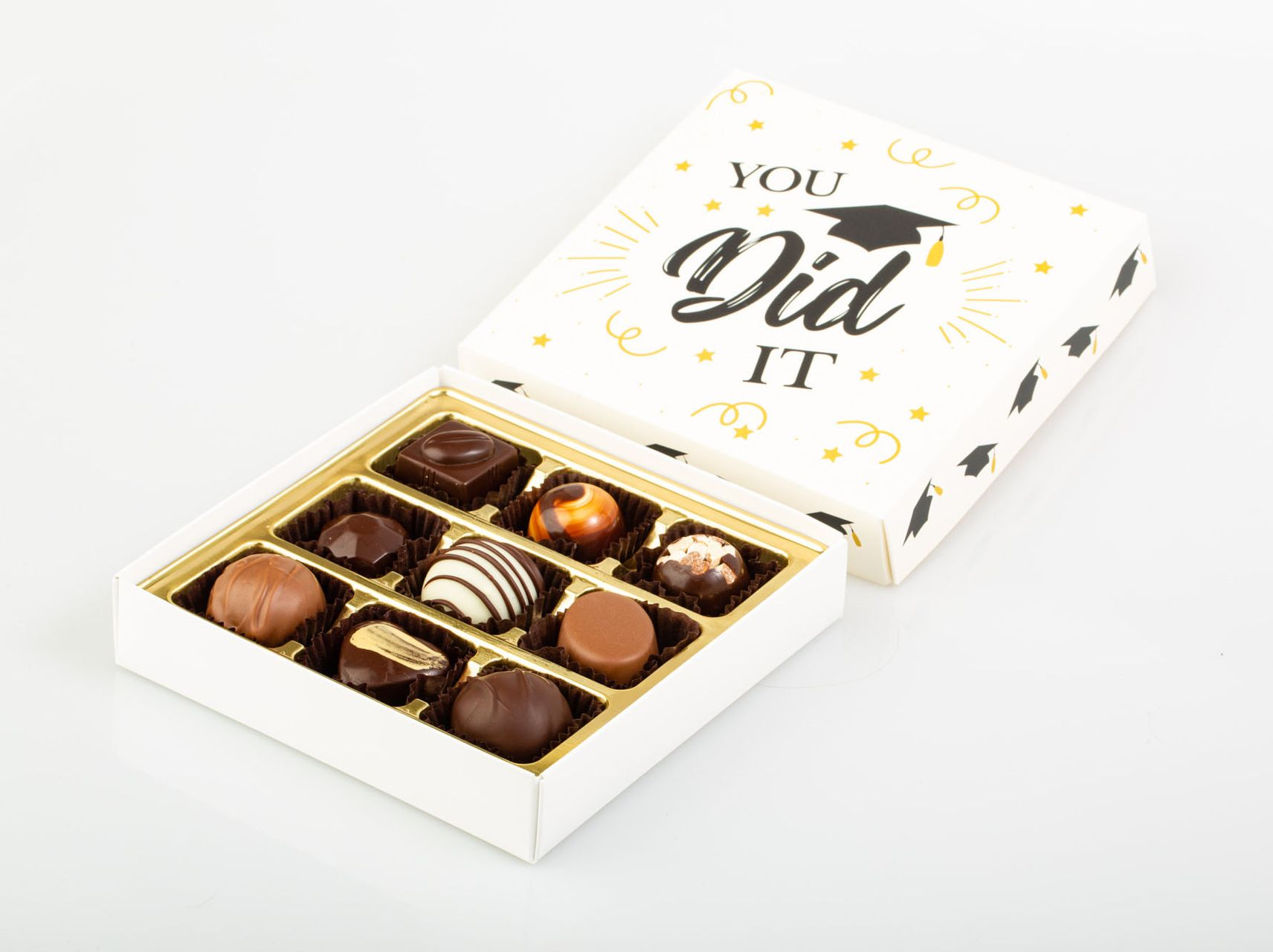 Open box of assorted chocolates with a “You Did It” lid on a white background