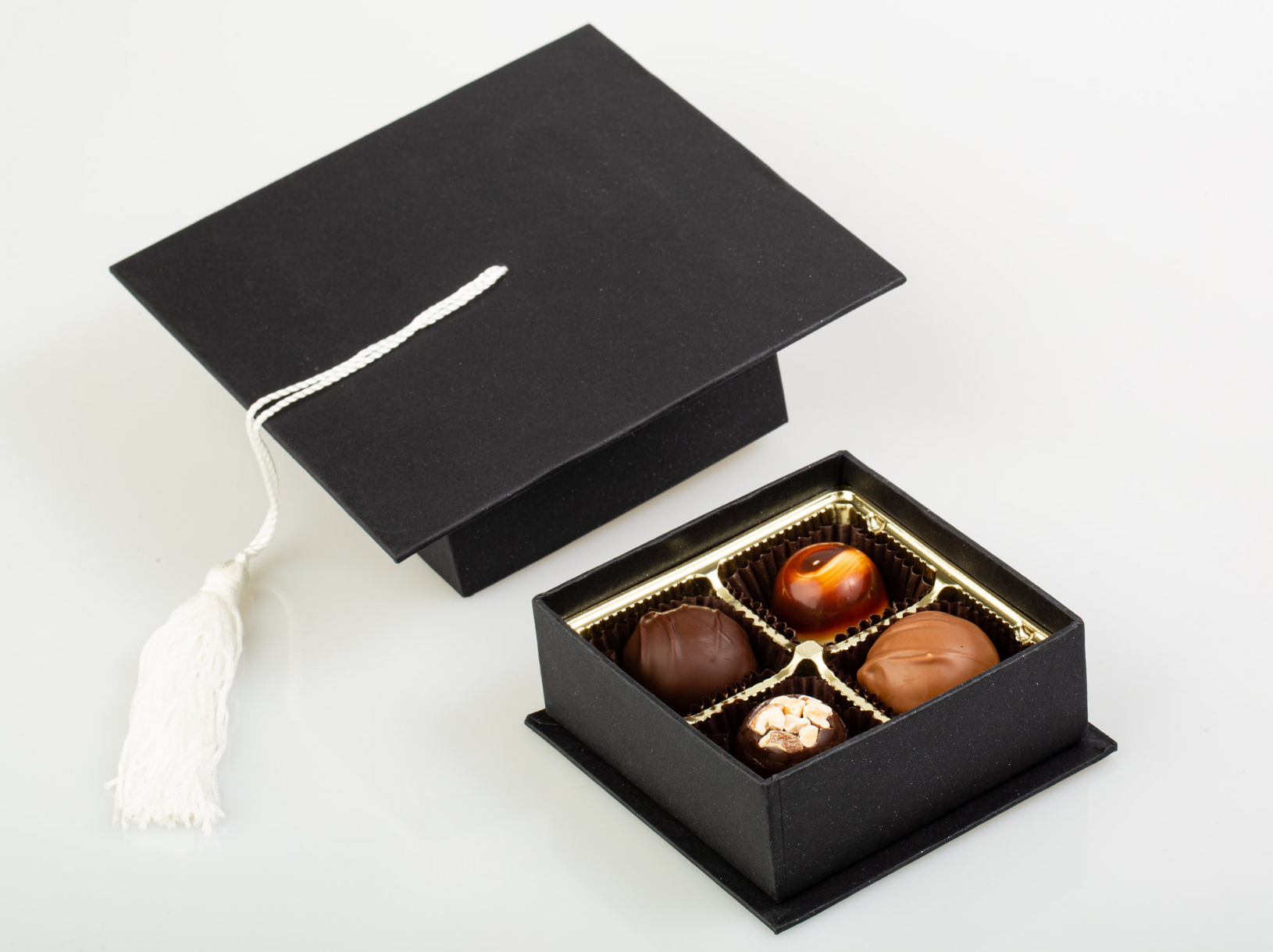 Black gift box with a white tassel lid, open to reveal assorted chocolates inside.