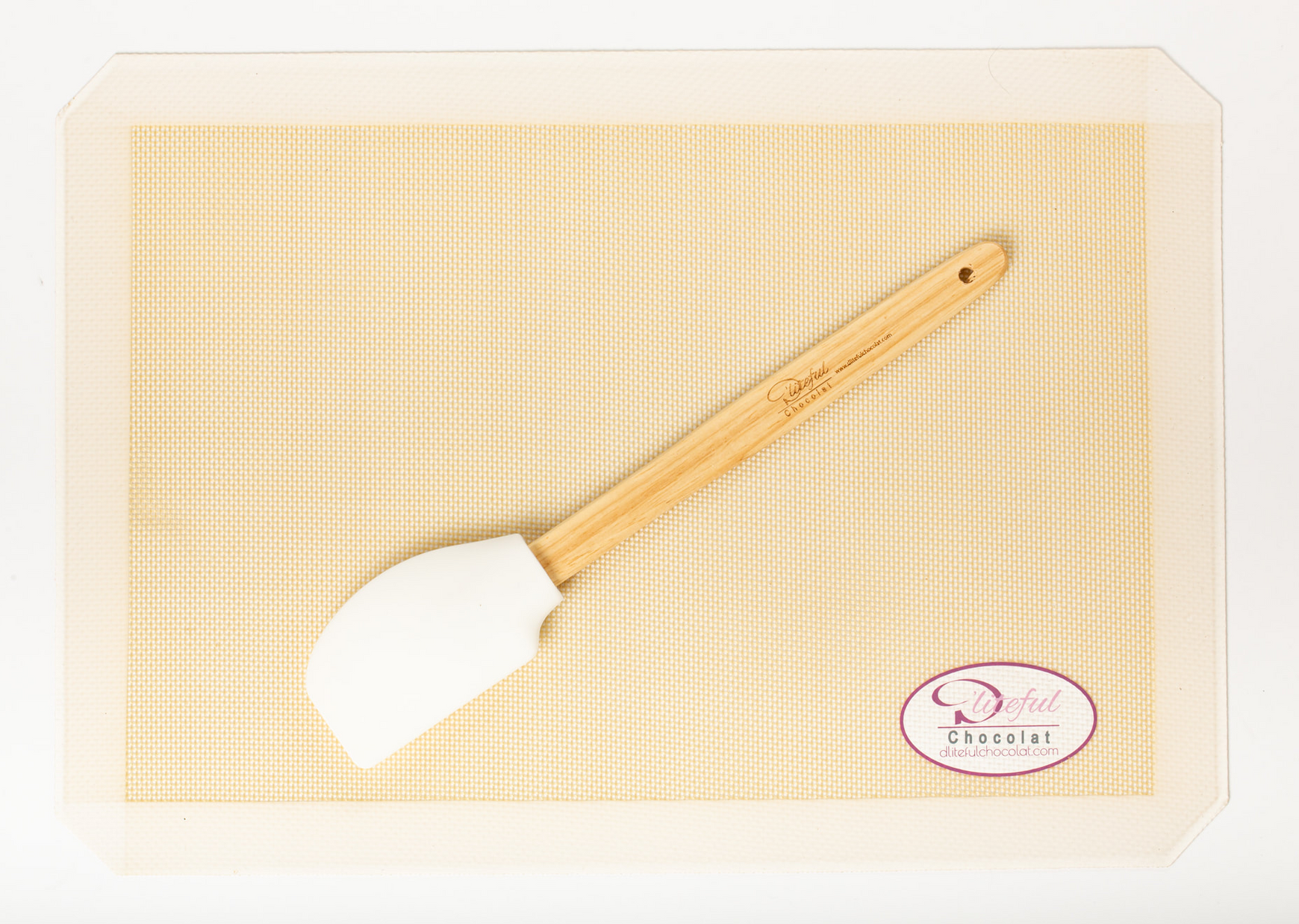 White silicone spatula with a wooden handle on a beige woven placemat, packaged in clear plastic.