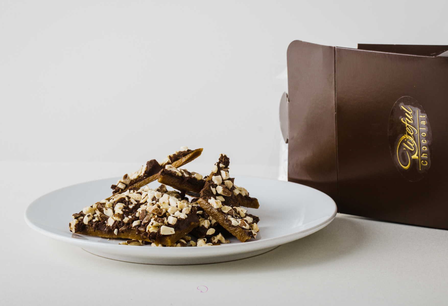 White plate of chocolate bark on a light surface beside a brown gift box.