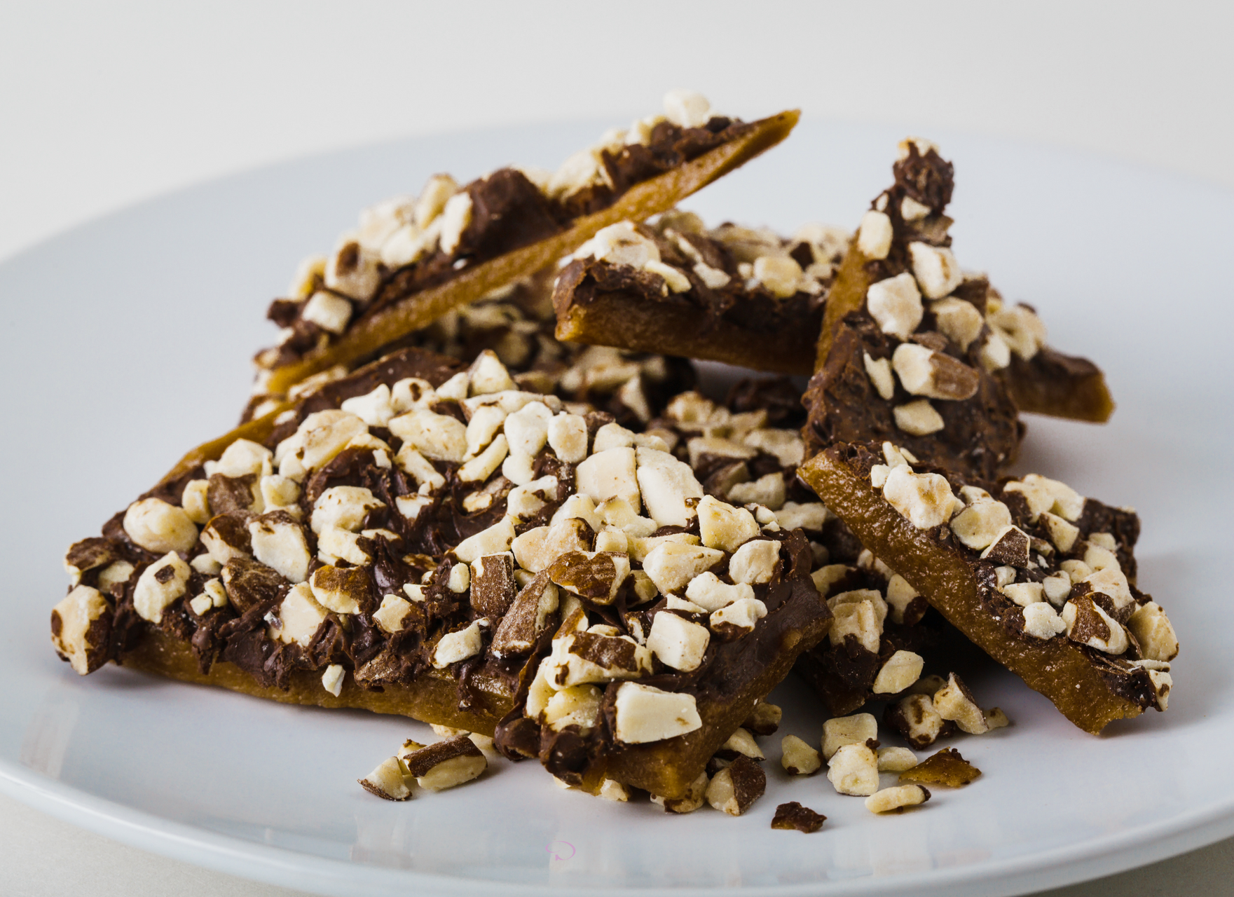 White plate of chocolate bark on a light surface beside a brown gift box.