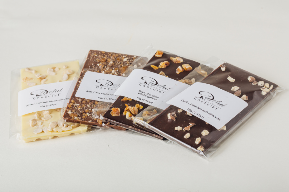 Four packaged chocolate bark varieties with nuts and fruit on a white background