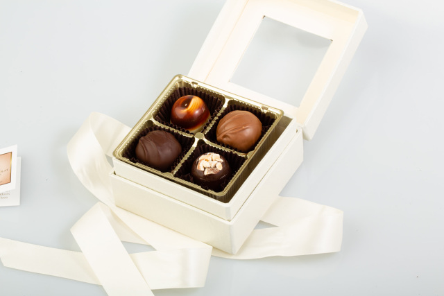 Open white chocolate gift box with four assorted chocolates on a white surface