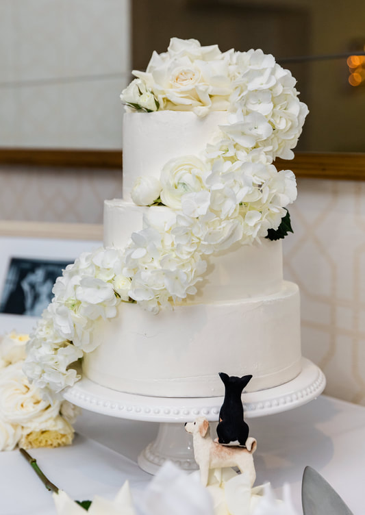 Two-tier white wedding cake with cascading white flowers and a small black cat topper
