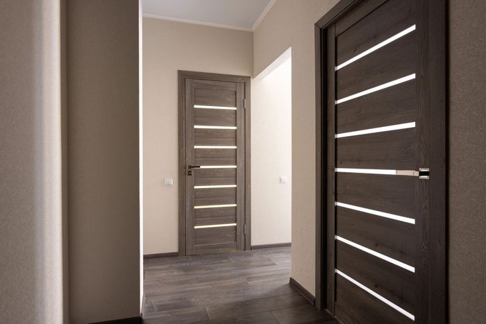 Corridoio interno con tre porte grigie, alcune aperte, pareti beige e pavimento scuro.