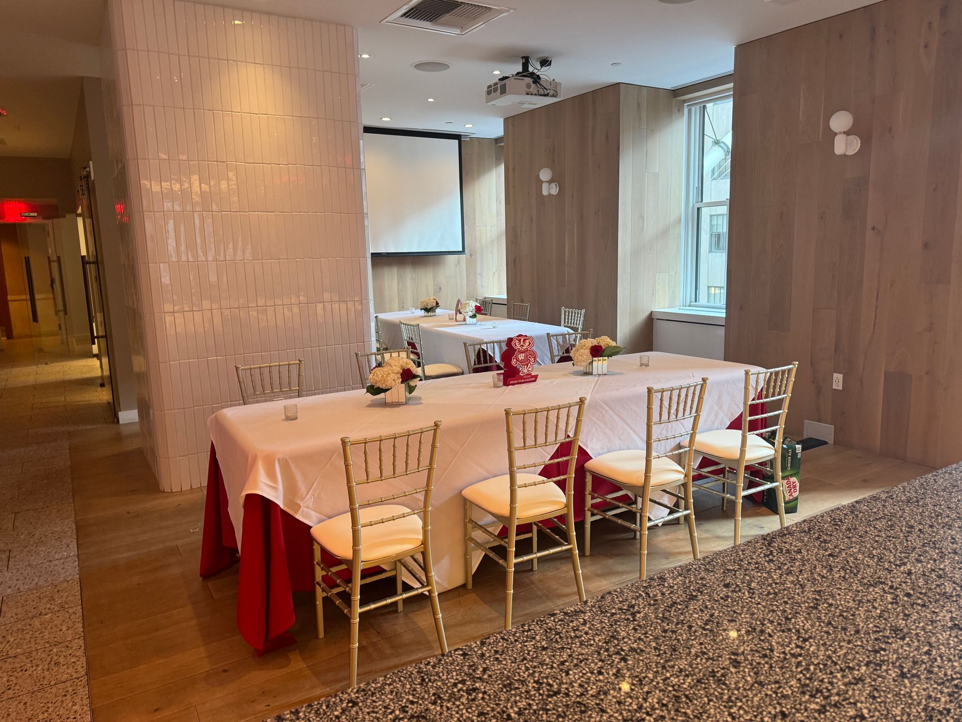 A long table and chairs in a room with a projector screen.